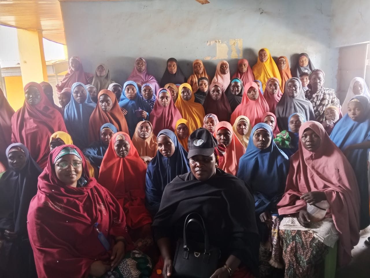 A large group of women in colorful headscarves seated together indoors
