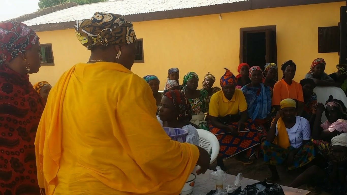 A trainer in a yellow shawl demonstrating to a seated group of women